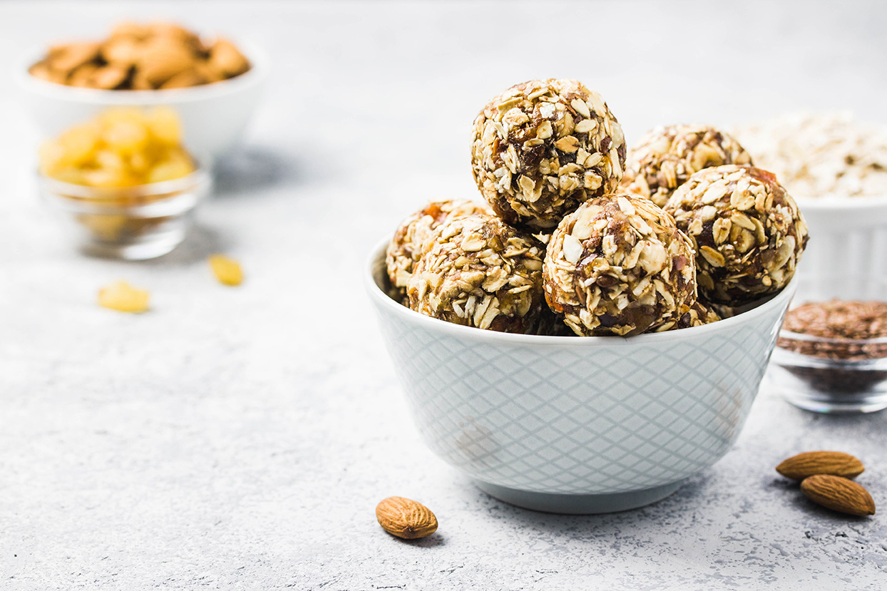 A bowl of no-bake protein balls sits on a table surrounded by ingredients.